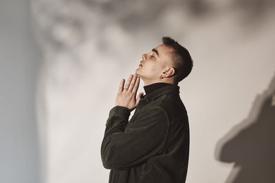 Side view of man with hands clasped by white background in studio