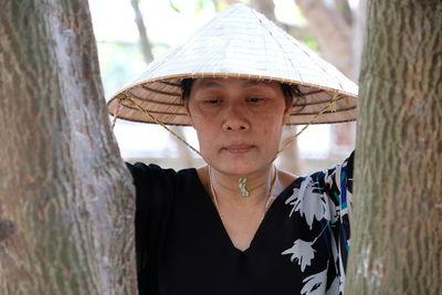 Mature woman wearing asian style conical hat by tree in forest