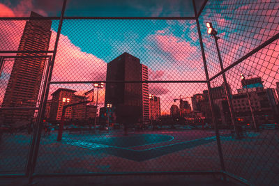 Basketball court seen through fence in city during sunset