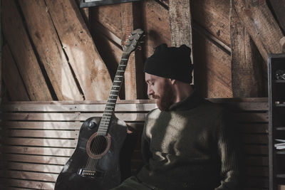 Young man sitting by guitar against wall