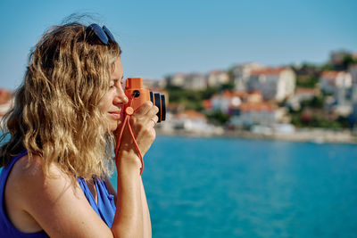 Side view of young woman photographing sea against sky