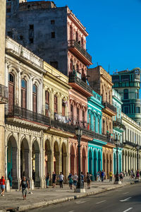 People on street by buildings in city against sky