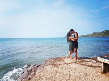 Full length of young couple kissing on beach against sky