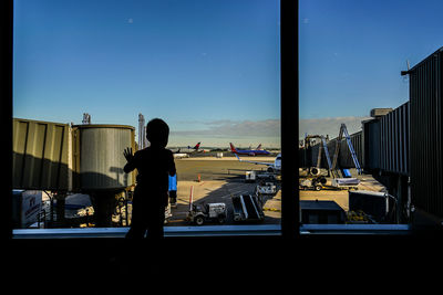 Rear view of man standing by airplane window against sky