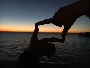 Close-up silhouette hands forming shape on beach during sunset