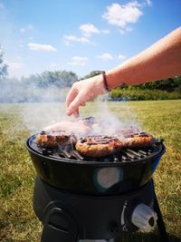 Man preparing food on barbecue grill against sky