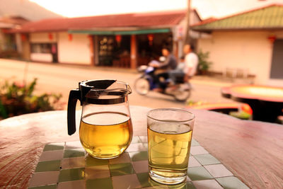 Drink in glass and jar on table with people on motorcycle in background