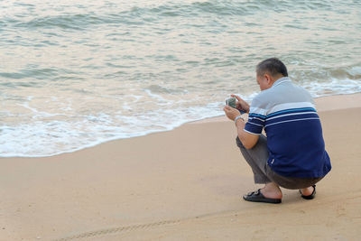 Rear view of man photographing on mobile phone at beach