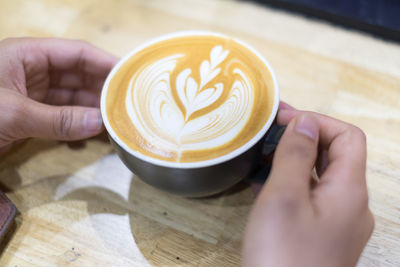 Close-up of hand holding coffee cup on table