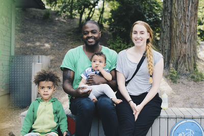 Portrait of smiling family sitting on retaining wall at park