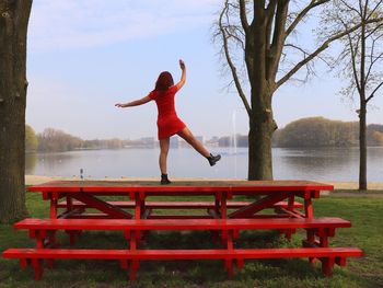 Full length of woman walking on bench by lake against sky