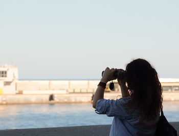 Rear view of woman looking sea through binoculars against sky