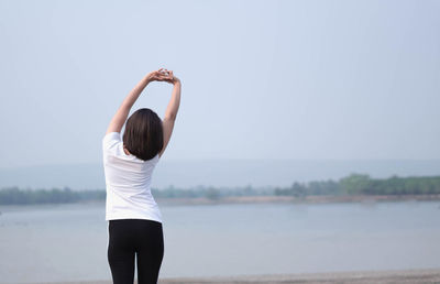 Rear view of woman standing by lake against sky