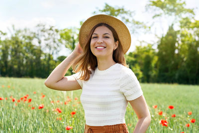 Beautiful young woman with hat posing in wheat field with poppy flowers and looking at camera