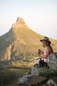 Woman sitting on rock against mountain against sky