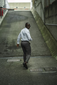 Back view of african american male entrepreneur in formal clothes and sunglasses with cellphone looking over shoulder in town