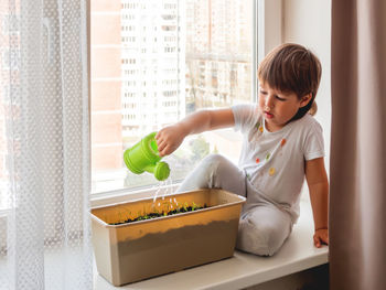 Toddler boy waters  seedlings on windowsill . little child with  watering can. kid's first duties.