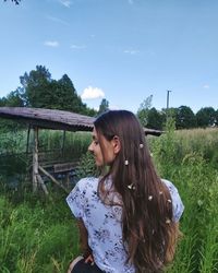Young woman looking away while standing on field against sky