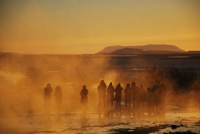 Silhouette people standing by hot spring against sky during sunset