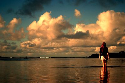 Man standing in sea against sky during sunset