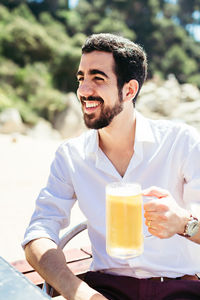 Portrait of smiling man with drink sitting outdoors