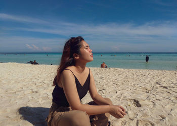 Young woman sitting on beach against sky