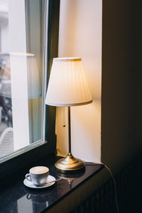 Cup of coffee sitting by the window next to a lamp