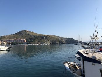 Sailboats moored at harbor against clear blue sky