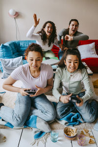 Cheerful multiracial female friends playing video game in living room at home