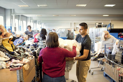 Man assisting woman in holding plastic while volunteers working at workshop