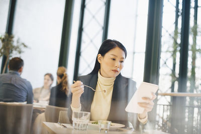 Confident businesswoman using digital tablet while eating lunch at cafeteria in office