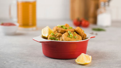 Golden chicken nuggets in a red bowl, sprinkled with green onions and a lemon wedge. pub menu