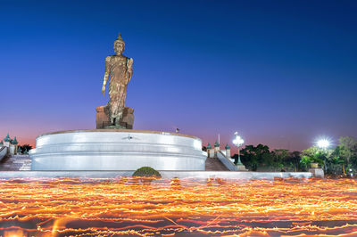 Statue by illuminated fountain against clear sky at night