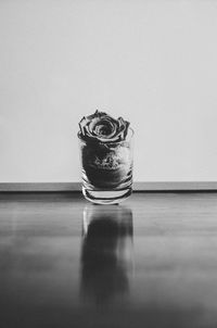 Rose in glass jar on hardwood floor against wall