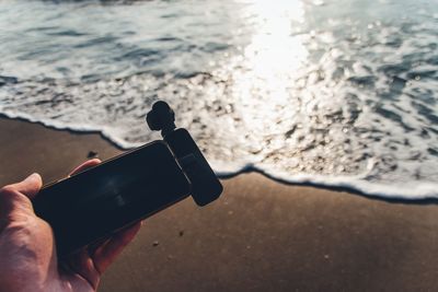 Cropped hand of person holding smart phone at beach during sunset