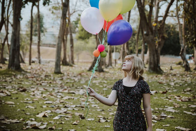 Woman looking away while holding balloons against trees