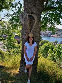 Portrait of smiling young woman standing on tree trunk