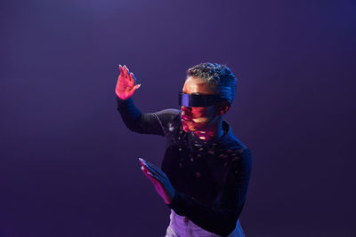 African american martial female with short hair in trendy vr goggles standing on purple background with outstretch arms in studio