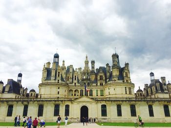 Tourists in front of building against cloudy sky