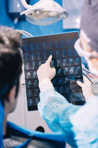 Cropped image of dentist showing x-ray to male patient in clinic