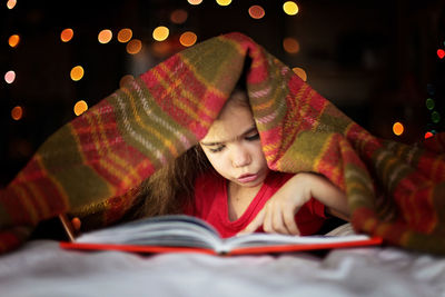 Cute girl reading book while lying on bed at home