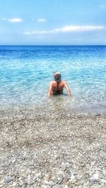 Rear view of woman sitting on shore at beach