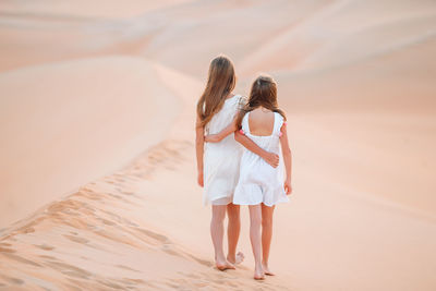 Rear view of women walking on sand at beach