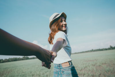 Cropped image of friend holding woman hand on field against sky