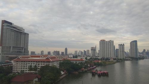 Buildings by river against sky in city