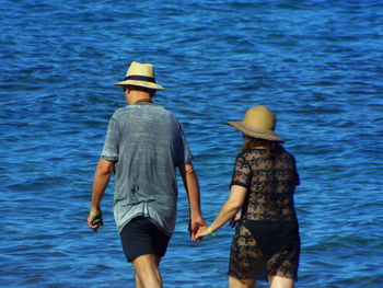 Rear view of couple walking at beach against sea