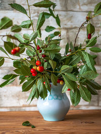 Summer bouquet with sprigs of cherries with berries in a blue ceramic vase in a rustic kitchen