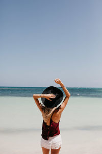 Woman in hat standing at beach against clear sky in sunny day