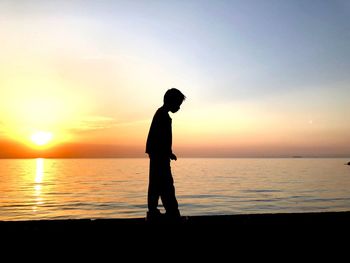 Silhouette man standing on beach against sky during sunset