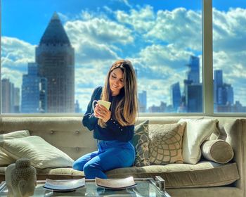 Full length of woman sitting on building in city against sky